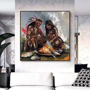 Op de afbeelding: Een schilderij van een Indiaans gezin dat rond een vuur zit. De vader draagt een hoofdtooi, de moeder houdt een kind vast en het vuur brandt fel. Op de voorgrond zijn houtblokken te zien.