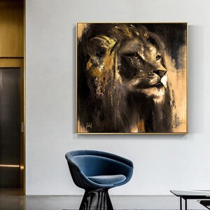 Op de afbeelding: Een vierkant wandkunstwerk met een gedetailleerd schilderij van een leeuwenkop in profiel. Het kunstwerk gebruikt een palet van zwart, donkerbruin en metallic goudtinten met zichtbare penseelstreken, omlijst door een dunne gouden rand. Een handtekening is zichtbaar.