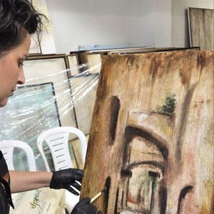 May include: A rectangular canvas painting on an easel featuring a textured, earth-toned depiction of an arched stone corridor. The artwork uses shades of brown, tan, and muted red to create depth, with dark brushstrokes defining the architectural arches.