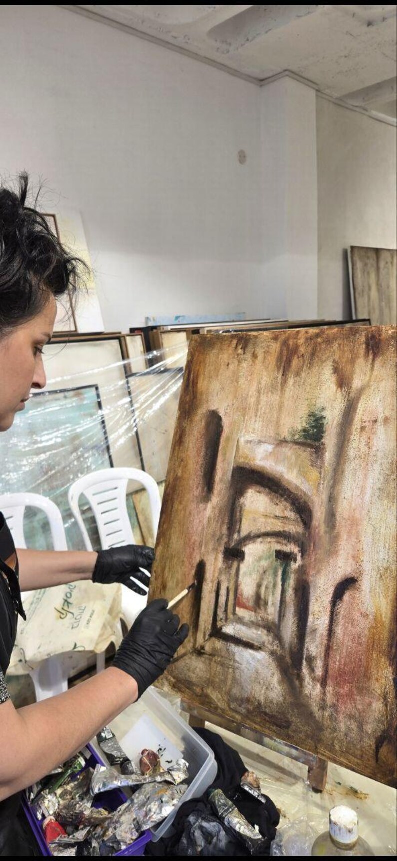 May include: A rectangular canvas painting on an easel featuring a textured, earth-toned depiction of an arched stone corridor. The artwork uses shades of brown, tan, and muted red to create depth, with dark brushstrokes defining the architectural arches.