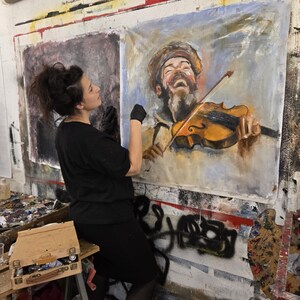 Puede incluir: Una pintura grande sobre lienzo rectangular que presenta el retrato de una persona con barba que lleva un sombrero y toca el viol&iacute;n. La obra utiliza pinceladas expresivas en tonos marrones, amarillos y azules, representando al sujeto con la boca abierta.