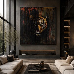 May include: A large square wall art piece featuring a detailed tiger face emerging from a dark, textured background with streaks of black, orange, and red paint. The artwork is framed in a thin black border and displayed on a dark gray wall.