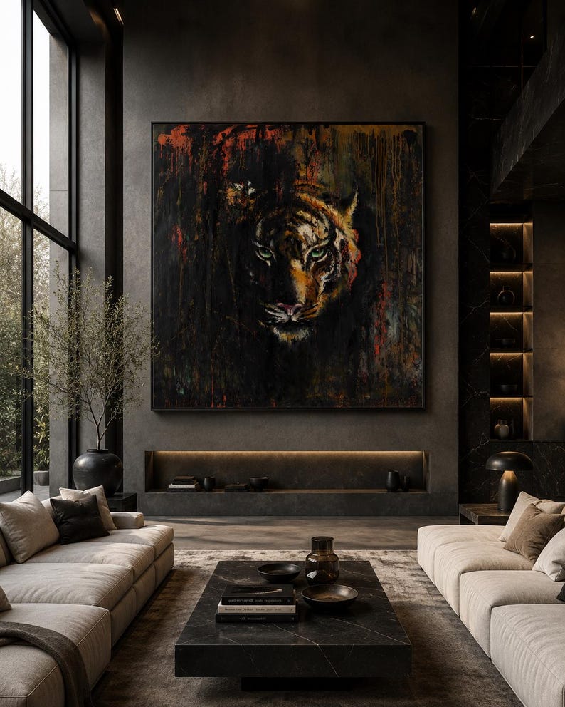 May include: A large square wall art piece featuring a detailed tiger face emerging from a dark, textured background with streaks of black, orange, and red paint. The artwork is framed in a thin black border and displayed on a dark gray wall.