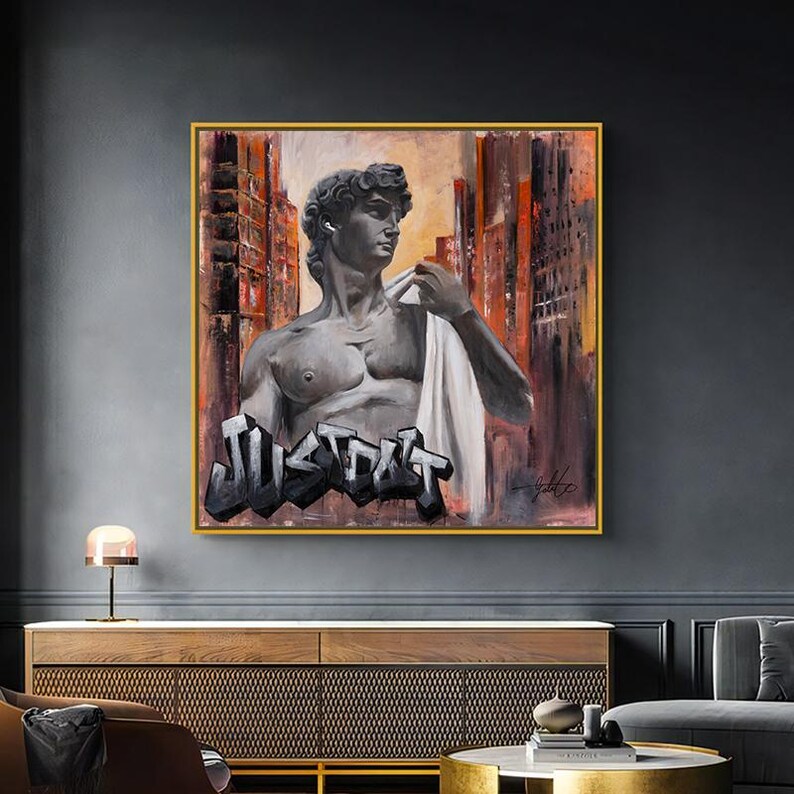 May include: A framed canvas wall art piece featuring a greyscale bust of Michelangelo's David wearing a white earbud. The figure is set against an abstract urban background with orange and brown tones, with the graffiti-style text JUST DO IT below.