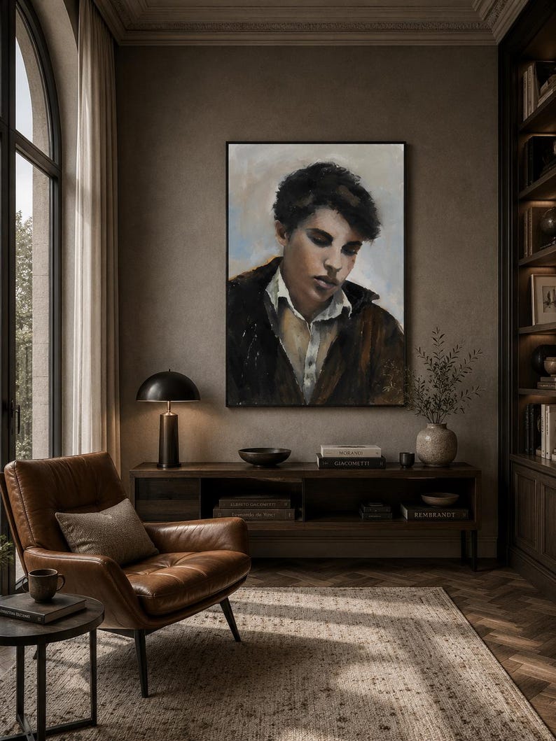 May include: A framed oil painting depicting a portrait of a person with dark hair, wearing a white collared shirt under a dark brown jacket, set against a muted background with soft blue and beige tones, displayed in a vertical rectangular frame.