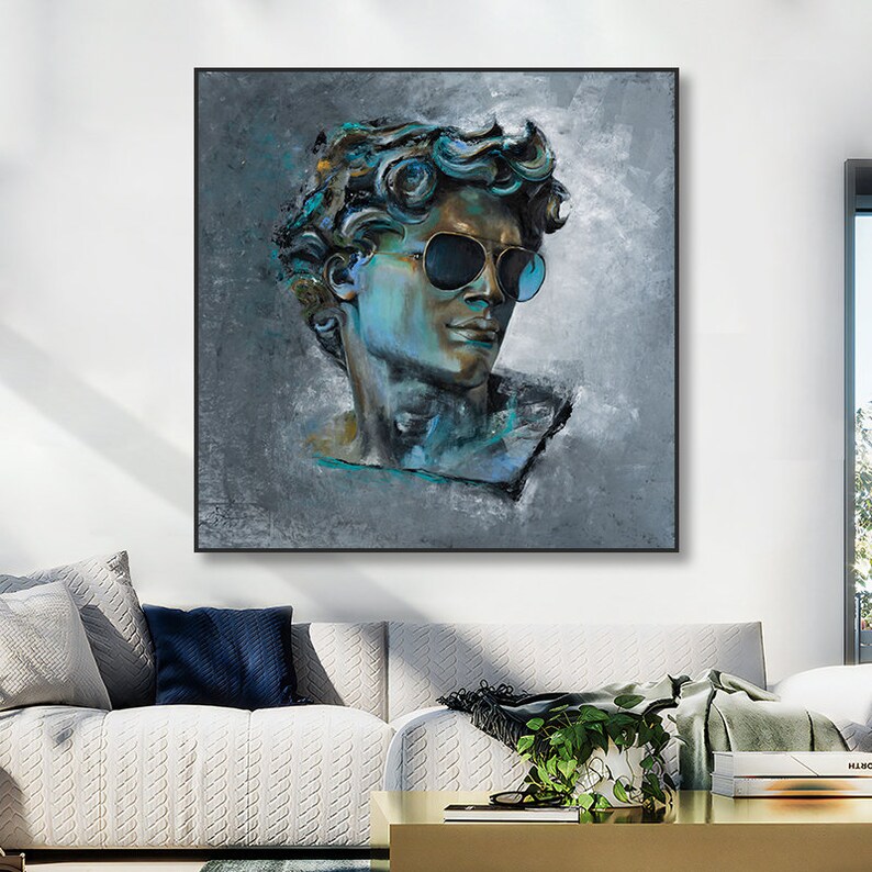 K&ouml;nnte beinhalten: Ein quadratisches Wandbild mit einem texturierten, malerischen Portr&auml;t einer klassischen m&auml;nnlichen B&uuml;ste, die eine dunkle Pilotenbrille tr&auml;gt. Das Kunstwerk verwendet eine Palette aus tiefen Blau-, T&uuml;rkis- und Graut&ouml;nen auf einem grauen Hintergrund.