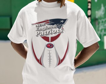 May include: White t-shirt featuring the New England Patriots logo and team name. The design includes a football shape with red and white accents. The shirt is a classic crew neck style.