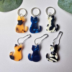 May include: Six cat-shaped stitch markers, three in tortoise shell, three in blue and white. Each marker has a silver ring and a safety pin.
