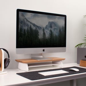 Peut inclure: Un support d'écran d'ordinateur en bois et blanc avec une étagère inférieure. Le support est sur un bureau blanc avec un tapis de souris noir et un clavier blanc.