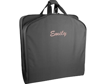 May include: A charcoal gray garment bag featuring a top handle and a central hook for hanging. The name Emily is embroidered in a light pink script font on the front center of the bag. The bag has a structured rectangular shape with rounded corners.
