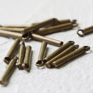 May include: A group of antique gold-toned metal bead caps with a small loop at one end. The bead caps are about 1 inch long.