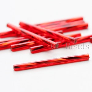 May include: A pile of red glass beads, each bead is a long, thin cylinder with a slightly twisted design. The beads are arranged in a random pattern, with some overlapping.