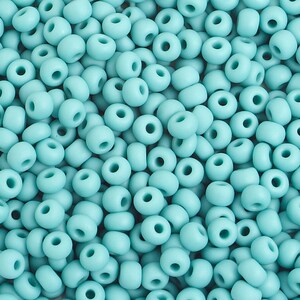 Pu&ograve; includere: Una vista ravvicinata di una grande quantit&agrave; di piccole perline rotonde color turchese. Le perline sono tutte della stessa dimensione e forma, e sono disposte in uno schema casuale.