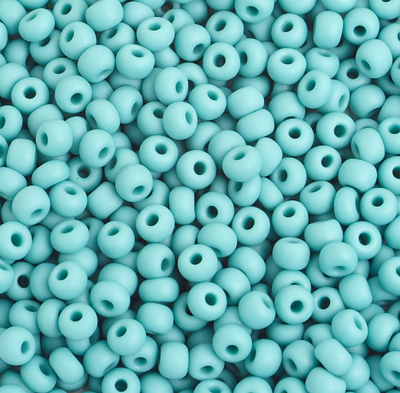 Pu&ograve; includere: Una vista ravvicinata di una grande quantit&agrave; di piccole perline rotonde color turchese. Le perline sono tutte della stessa dimensione e forma, e sono disposte in uno schema casuale.
