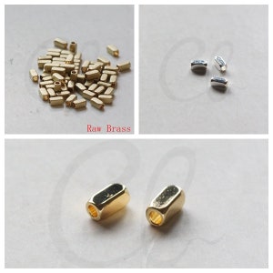 May include: A close-up of two gold-coloured metal end caps for jewellery making. The end caps are cylindrical with a hole in the centre. The image also shows a pile of smaller, raw brass end caps.