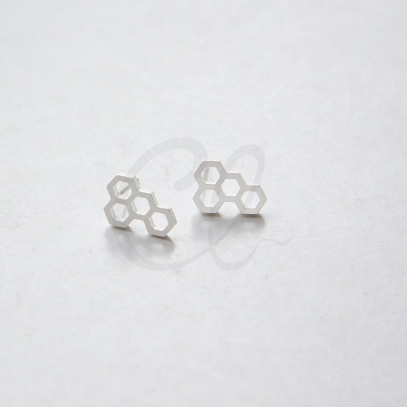 May include: A pair of silver honeycomb-shaped stud earrings.
