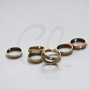 May include: A group of six raw brass rings with two small holes in each ring. The rings are stacked on top of each other.