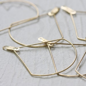 May include: A set of four gold geometric hoop earrings. The earrings are made of thin wire and have a simple, modern design.