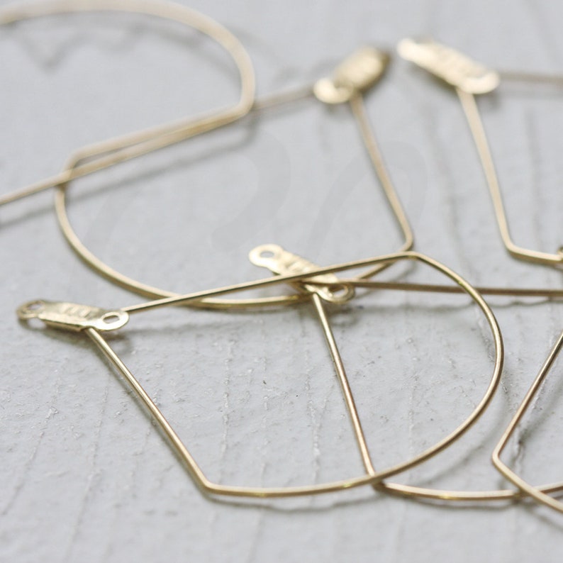 May include: A set of four gold geometric hoop earrings. The earrings are made of thin wire and have a simple, modern design.