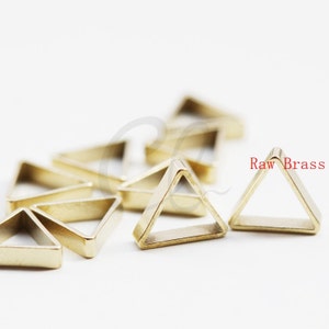 Pode incluir: Um grupo de pequenos anéis de metal de forma triangular de cor dourada. Os anéis estão dispostos em uma pilha solta sobre uma superfície branca. O texto "Raw Brass" é visível na imagem.