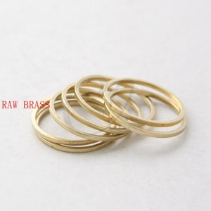 May include: A set of five gold-coloured metal rings, stacked on top of each other.  RAW BRASS is written in red text on the left side of the image.