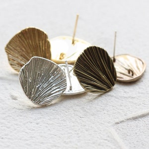 Op de afbeelding: Een verzameling metalen oorstekers in verschillende afwerkingen, waaronder goud, zilver en brons. De oorbellen hebben een textuur, waaiervormig ontwerp. De pinnen zijn zichtbaar, wat aangeeft dat ze bedoeld zijn om in doorboorde oren te worden gedragen. Gepresenteerd op een witte ondergrond.