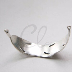 May include: Silver-toned metal bracelet with a decorative, openwork design. The bracelet is curved and has a smooth, polished finish.