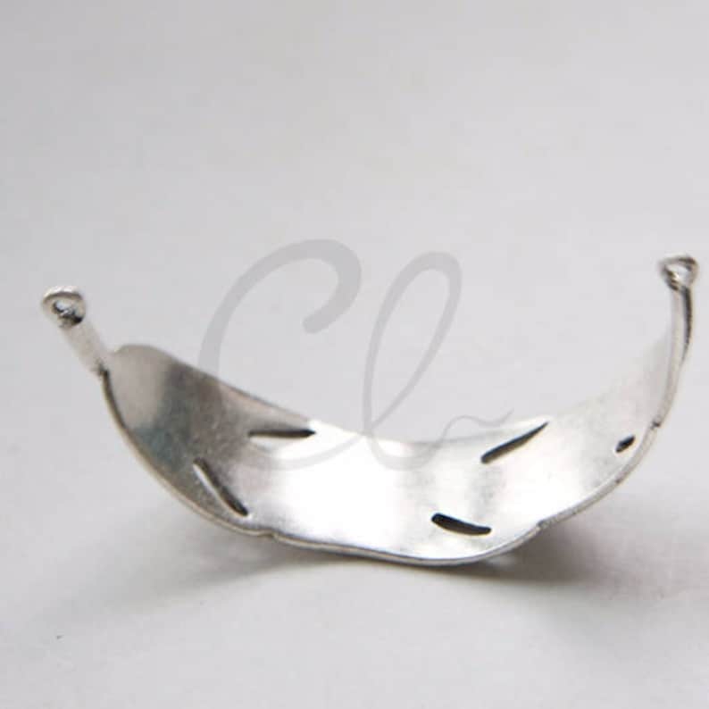 May include: Silver-toned metal bracelet with a decorative, openwork design. The bracelet is curved and has a smooth, polished finish.