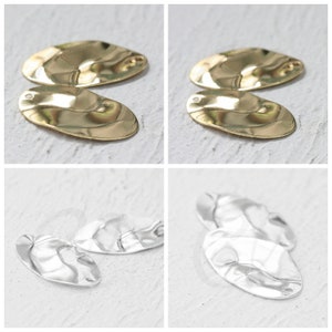 Op de afbeelding: Twee paar ovale metalen oorbellen. Het ene paar is goud en het andere is zilver. De oorbellen hebben een golvend, getextureerd oppervlak.