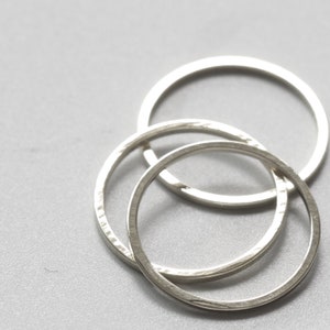 May include: Three silver rings interlocked together. The rings are smooth and have a slightly textured surface.