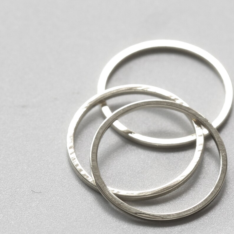 May include: Three silver rings interlocked together. The rings are smooth and have a slightly textured surface.