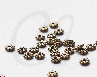 May include: A scattering of small, antique gold-toned metal beads with a flower-like design. Each bead has a small hole in the center for stringing.