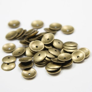 Puede incluir: Un montón de cuentas de metal de color dorado antiguo. Las cuentas son redondas y tienen un centro elevado. Son perfectas para hacer joyas u otros proyectos de artesanía.