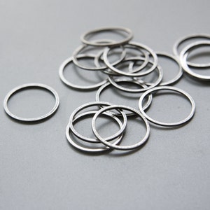 May include: A pile of silver metal rings, some stacked on top of each other. The rings are all the same size and shape, and they have a smooth, polished finish.