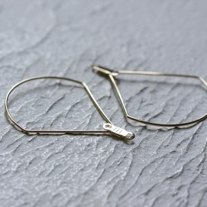 May include: A pair of gold hoop earrings with a geometric teardrop shape.