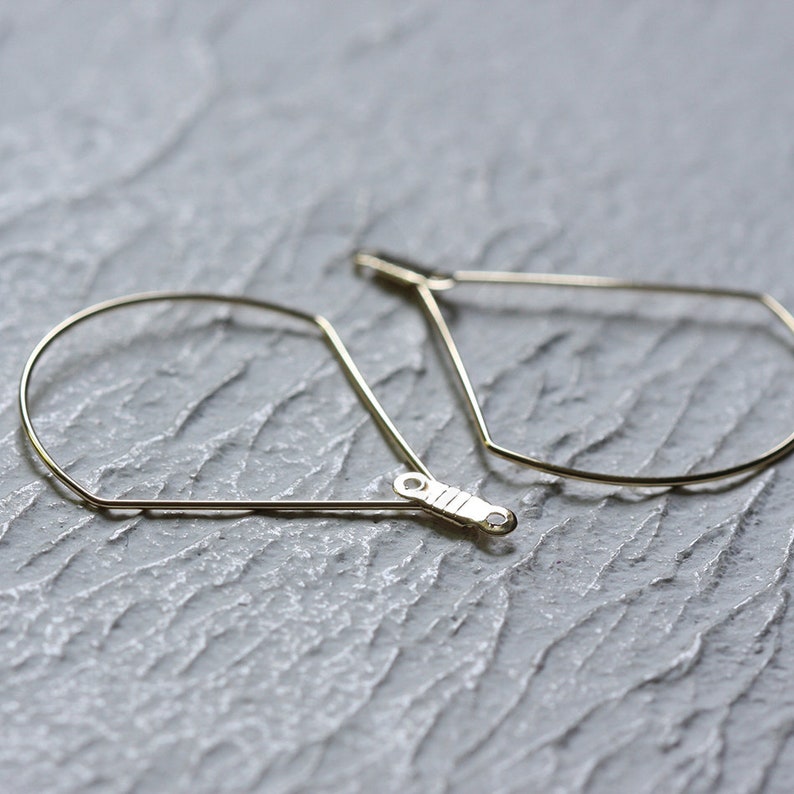 May include: A pair of gold hoop earrings with a geometric teardrop shape.