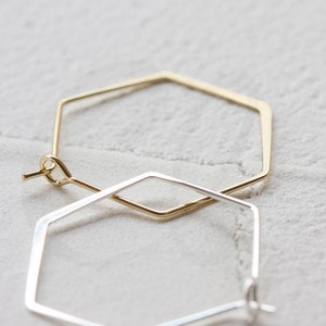 May include: A pair of geometric hoop earrings. One earring is gold and the other is silver. Both earrings are in the shape of a hexagon.