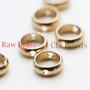 May include: A collection of small, round, gold-colored metal beads with a smooth finish and two holes on the sides. The text "Raw Brass" is printed in red and "CL Beads" is printed in gray across the image of these circular jewelry components.