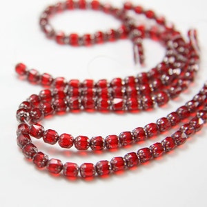 Puede incluir: Una hebra de cuentas de vidrio rojas con un diseño facetado. Las cuentas están enhebradas en un hilo transparente.