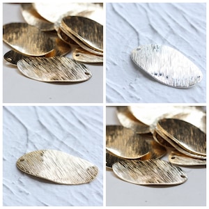 May include: A close-up of a pile of gold-colored metal oval shapes with a textured surface. The ovals have a small hole at each end. There is also a single silver-colored oval with the same texture and holes.