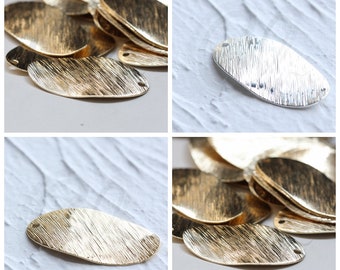 Pode incluir: Um close-up de uma pilha de formas ovais de metal dourado com uma superfície texturizada. Os ovais têm um pequeno furo em cada extremidade. Há também um único oval prateado com a mesma textura e furos.