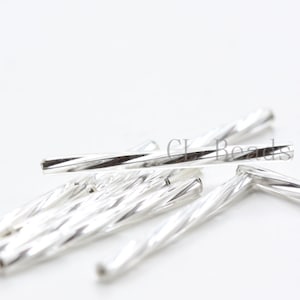 May include: Close-up of several silver-colored, twisted tube beads. The beads have a spiral design and are scattered against a white background. The text "CK Beads" is visible in the background.