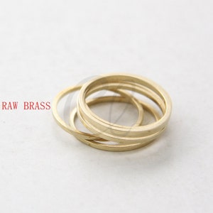 May include: Four gold-coloured metal rings stacked on top of each other. RAW BRASS is written in red text below the rings.