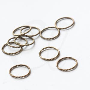 May include: A group of 10 small, gold-toned, twisted metal rings. The rings are scattered on a white surface.
