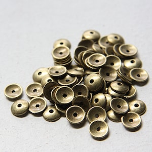 May include: A pile of small, round, gold-colored metal beads with a hole in the center. The beads are slightly domed and have a shiny finish.