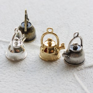 Könnte beinhalten: Eine Sammlung von Miniatur-Kessel-Anhängern in verschiedenen Metallausführungen: Silber, Gold und Bronze. Jeder Kessel hat einen Griff, einen Ausguss und einen Deckel, ideal für Schmuckherstellung oder Bastelprojekte.