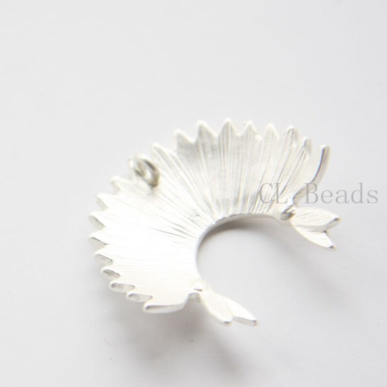 May include: Silver-toned metal pendant with a fan-shaped design. The pendant has a loop at the top for attaching to a chain or cord.