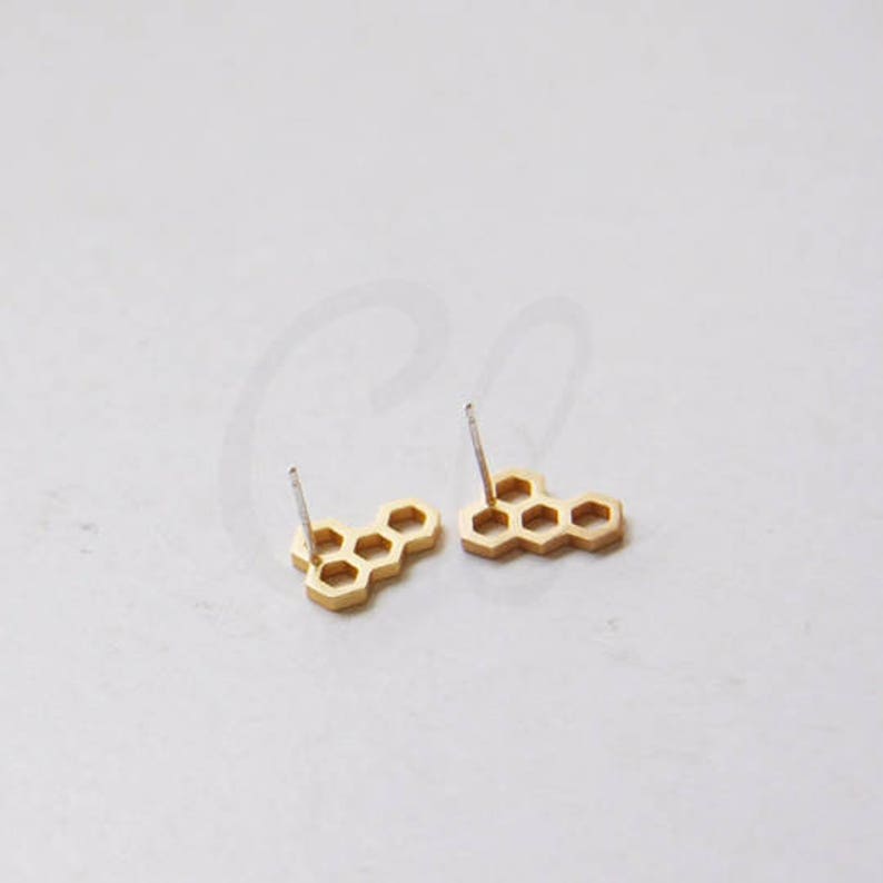 May include: A pair of gold honeycomb stud earrings. The earrings are made of metal and have a simple, geometric design.