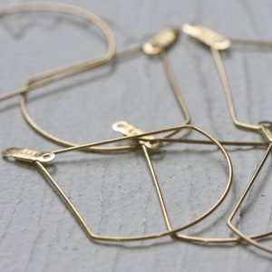May include: A set of four gold-toned metal hoops with geometric shapes. The hoops are made of thin wire and have a simple, modern design.