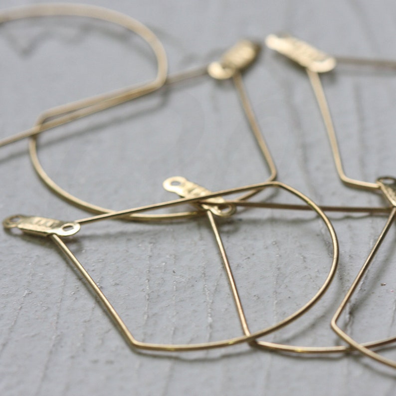 May include: A set of four gold-toned metal hoops with geometric shapes. The hoops are made of thin wire and have a simple, modern design.